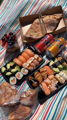 an assortment of sushi and other food items on a picnic blanket with sodas