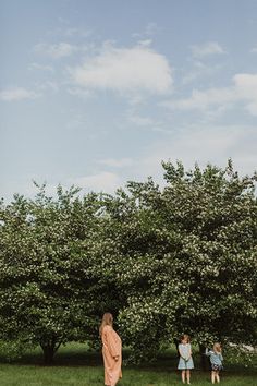 three children are standing in the grass near some trees