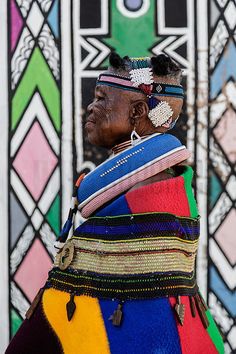 an old woman wearing colorful clothing and headdress in front of a stained glass window