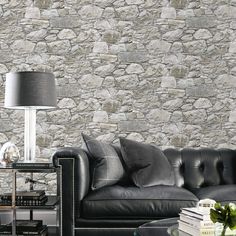 a living room with a black leather couch and coffee table in front of a stone wall