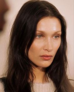 a woman with long dark hair and blue eyes wearing a white sweater is looking at the camera