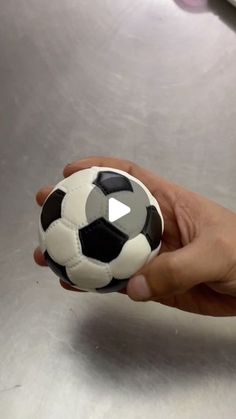 a hand holding a black and white soccer ball on top of a metal surface,