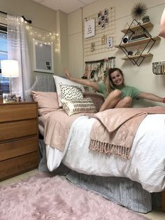 a woman sitting on top of a bed next to a pink rug and wooden dresser