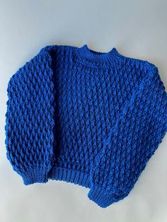 a blue knitted sweater laying on top of a white surface