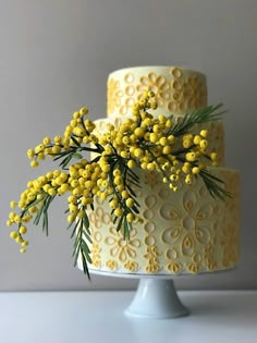 a three tiered cake with yellow flowers on the top and green leaves on the bottom