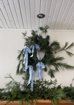 a wreath is hanging on the wall with blue ribbon and pine branches in front of it