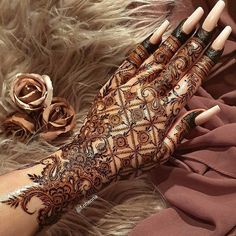 a woman's hand with henna on it and some flowers in the background