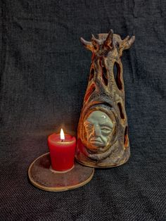 a candle holder with a face on it next to a lit candle