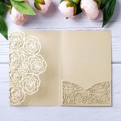 an open card with paper cut out and flowers on the side, next to pink roses