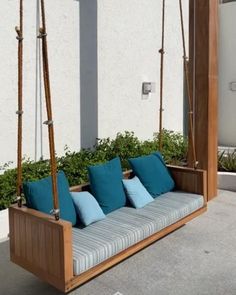 a wooden swing bed with blue pillows in front of a white wall and planters