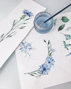 some watercolors are sitting on top of paper with blue flowers painted on them