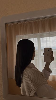 a woman taking a selfie with her cell phone in front of a window,