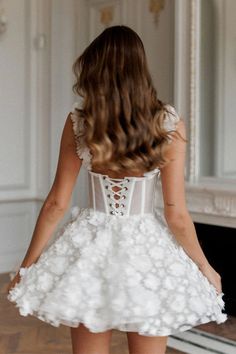 the back of a woman's dress with white flowers on it, standing in front of a fireplace