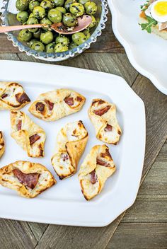 small appetizers are arranged on a platter with olives in the background