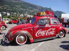 an old red car is parked in a parking lot with people standing around and looking at it