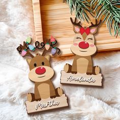 two wooden reindeer magnets sitting on top of a white fur covered floor next to a pine tree