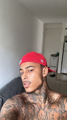 a man with tattoos on his chest wearing a red hat