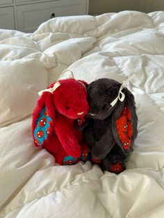 two stuffed animals sitting on top of a white bed covered in sheets and pillows,