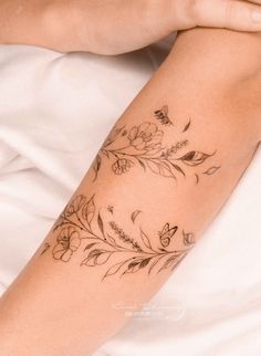 a woman's arm with flowers and leaves tattooed on her left arm, resting on a bed