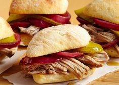 four sandwiches with meat, peppers and pickles on a cutting board next to bread