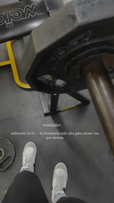 a person with white shoes standing next to a barbell on a gym floor in front of a bench