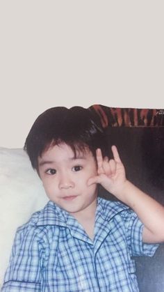 a young boy sitting on top of a couch holding his hand up in the air