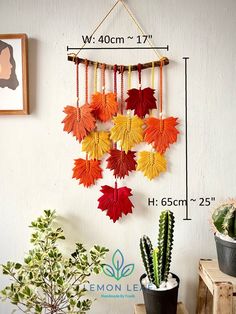 an arrangement of autumn leaves hangs on the wall next to a potted cacti