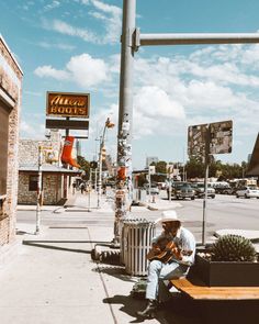 a man sitting on a bench next to a trash can with a guitar in his hand