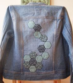 a denim jacket with an embroidered design on it sitting on top of a wooden chair