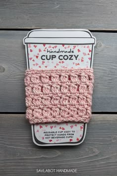 a pink crocheted cup cozy sitting on top of a wooden table next to a package