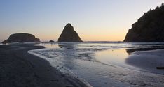 the sun is setting at the beach with some rocks in the water and people walking on the sand