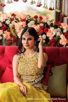 a woman sitting on top of a red couch wearing a yellow dress and gold jewelry