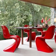 a dining room with red chairs and a table in front of a stone wall,