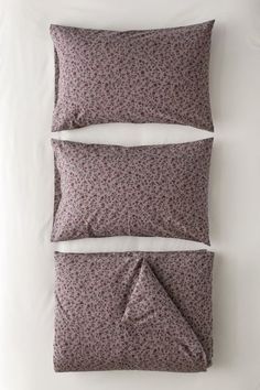 two pillows on top of each other in front of a white bed with purple flowers