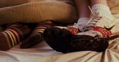 two pairs of shoes sitting on top of a bed next to a person's legs