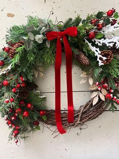 a christmas wreath hanging on the side of a wall with red ribbon and pine cones