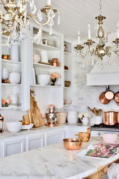 a kitchen filled with lots of white counter tops and gold chandelier hanging from the ceiling