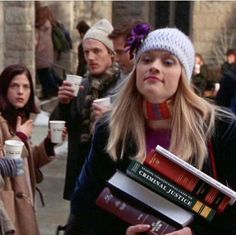 a woman holding books and drinking coffee while standing in front of a group of people