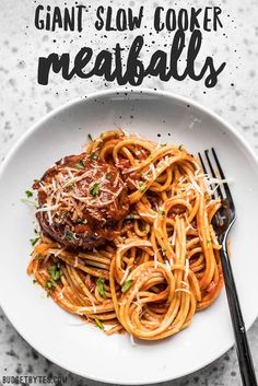 a white plate topped with pasta and meat next to a fork on top of a table