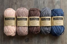 six skeins of soften denim yarn in various colors on a wooden surface