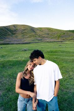 a young man and woman are standing in the grass with their arms around each other