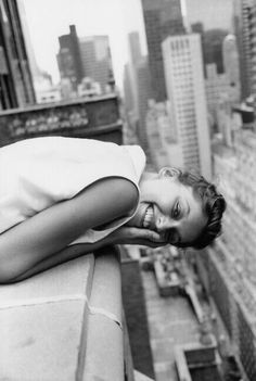 black and white photograph of a woman laughing on a city street with buildings in the background