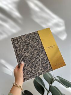 a person holding up a book in front of a plant with long thin lines on it