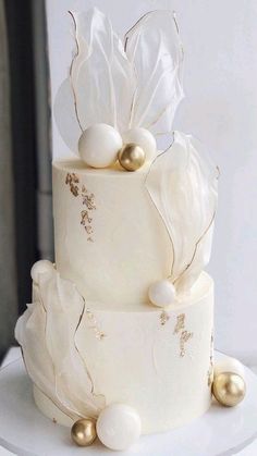 a three tiered cake with white frosting and gold decorations on it's side