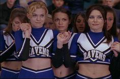 three cheerleaders posing for the camera in front of a group of people with their hands on their hips