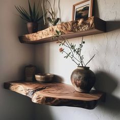 a wooden shelf with two vases on top of it and some plants in the corner