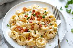 a white plate topped with macaroni and cheese covered in bacon next to a fork