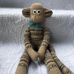 a knitted monkey sitting on top of a white bed with its eyes wide open