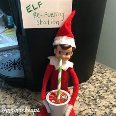 an elf is holding a drink with a straw in his hand and a sign that says elf re - fueling station