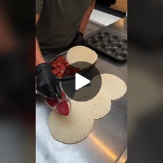 a person making food on top of a metal counter next to muffin tins